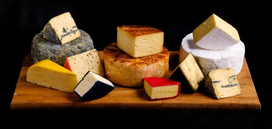 Assortment of artisan cheeses, including blue, hard, and soft varieties, beautifully displayed on a wooden board.