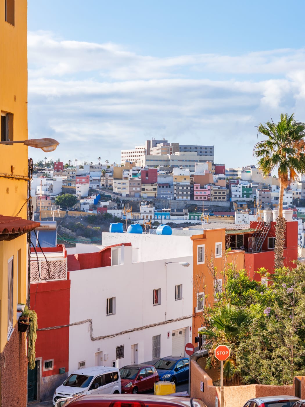 Cars parked on a steep street below colourful hillside houses in Las Palmas