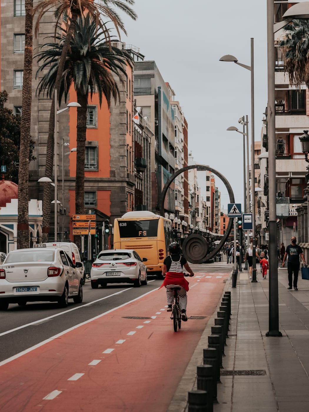 A yellow city bus, a taxi and a cyclist on a Las Palmas street, with signs pointing to the bus station and Triana
