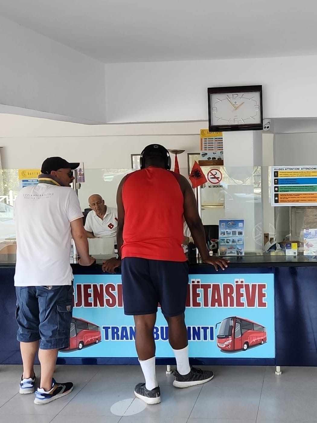 Des voyageurs achètent des billets de bus interurbains au guichet de Trans Butrinti