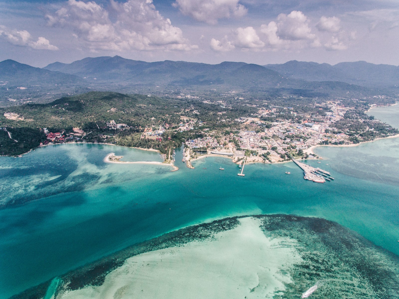 Aerial view of the Andaman coast: turquoise shallows, reef and a harbour town below forested hills