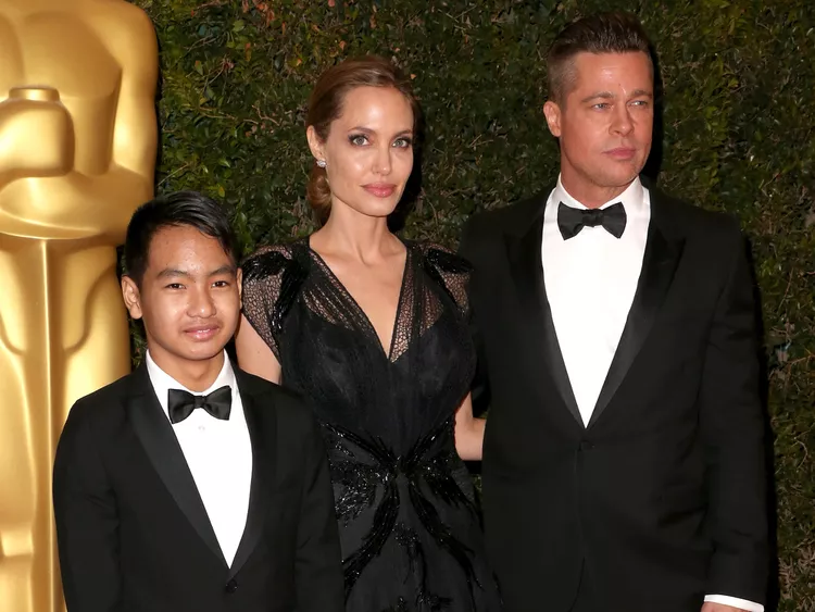 Maddox Jolie-Pitt, Angelina Jolie, and Brad Pitt posing together at an awards event, all dressed in formal black attire with bow ties.