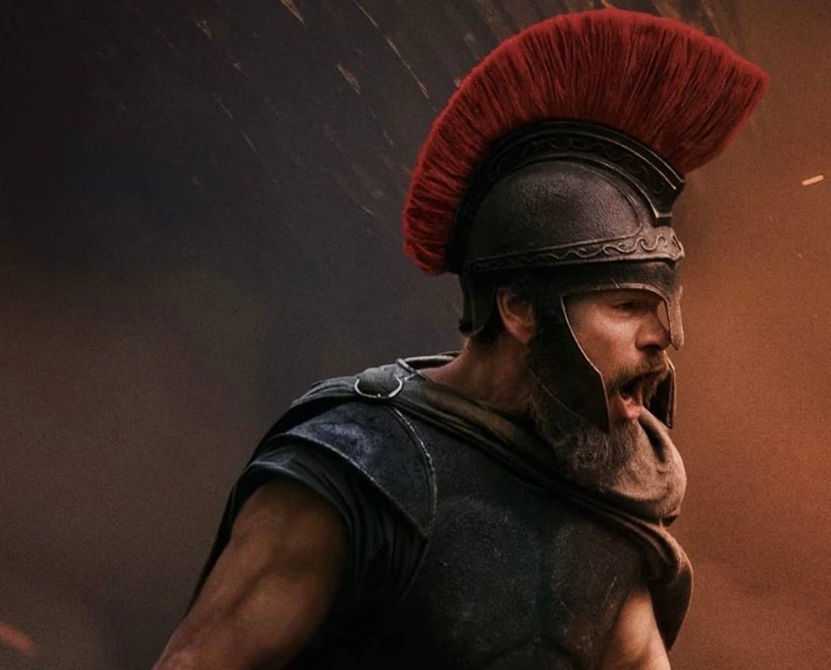 Matt Damon as Odysseus, in ancient Greek armour with a red-plumed helmet, shouting in a dramatic battle scene.
