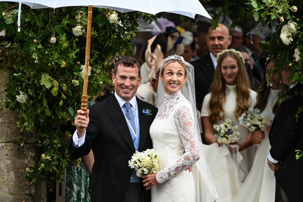 A newlywed couple shares an umbrella during their rainy wedding ceremony, surrounded by white flowers and wedding guests.