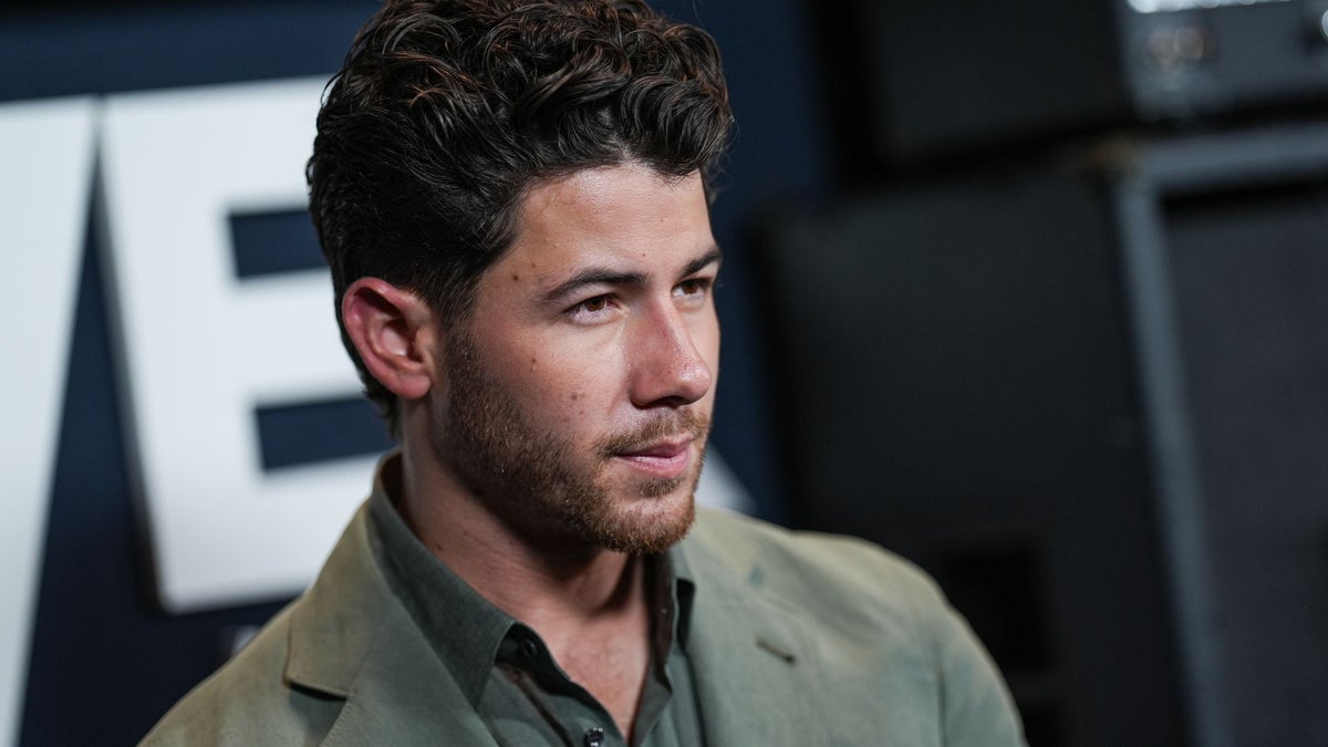 Nick Jonas wears a tan button-up shirt at what appears to be a professional event.