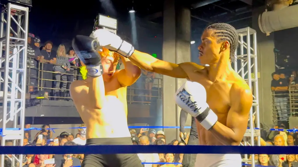 Knox Jolie (left) taking a punch from his opponent in a boxing match, with a crowd watching ringside.
