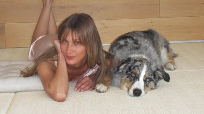Bella Hadid lying on the floor beside a Australian Shepherd dog, wearing a pink satin top.