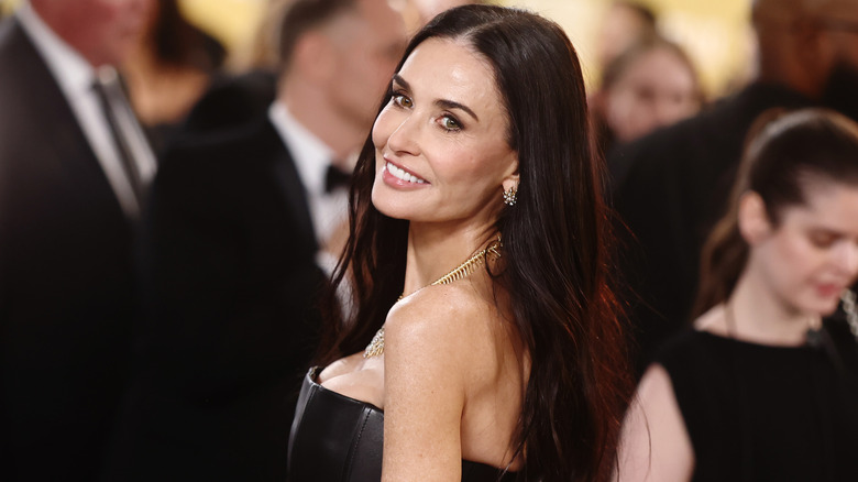 Demi Moore with long dark hair wearing a black strapless dress and gold jewelry at a formal event.