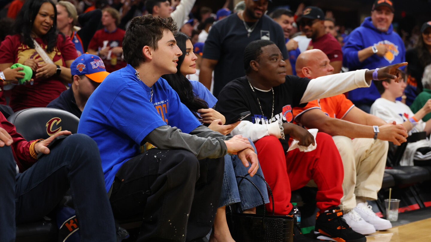 Timothée Chalamet, Kylie Jenner and Tracy Morgan blue and red team apparel sit courtside at a basketball game, watching the action intently.