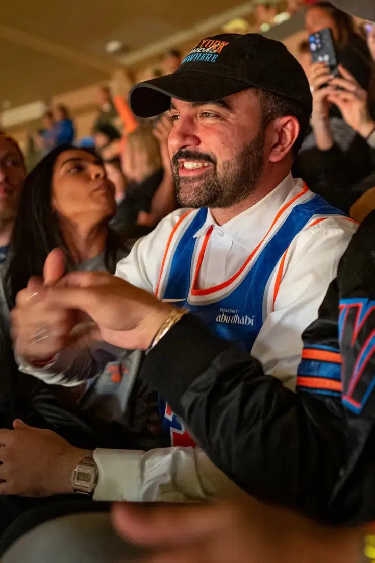 Zohran Mamdani wearing a New York Knicks jersey in the stands at a Knicks game.