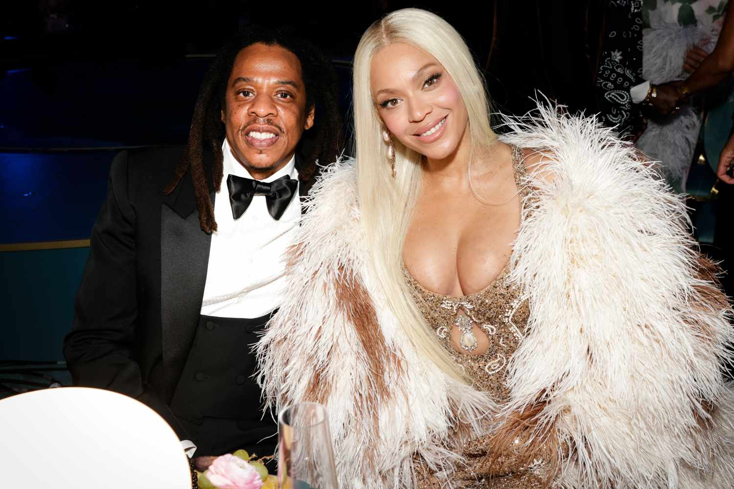 Jay-Z in a tuxedo and Beyoncé in a gold embellished gown with a white feather coat at a formal event.