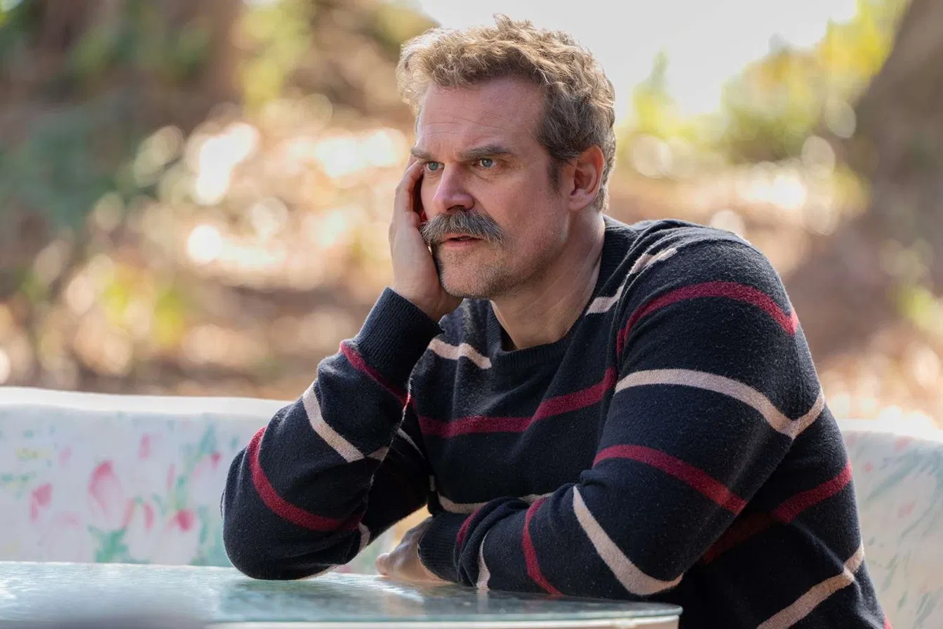 David Harbour in a striped sweater resting his head on his hand in a still from HBO's DTF St. Louis.