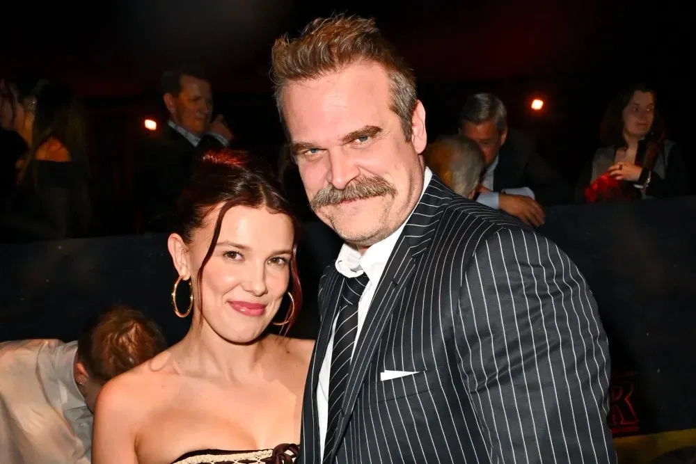 David Harbour in a pinstripe suit and Millie Bobby Brown in a strapless dress seated together at a cinema screening event.