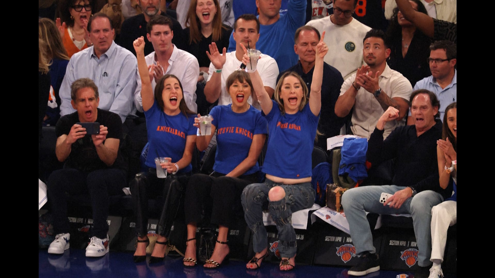 Excited fans wearing New York Knicks gear cheer courtside at Madison Square Garden during a game.