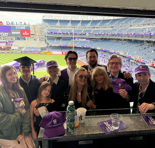 Kate Hudson's family posing together in a luxury box at a baseball stadium with purple seating visible behind them.