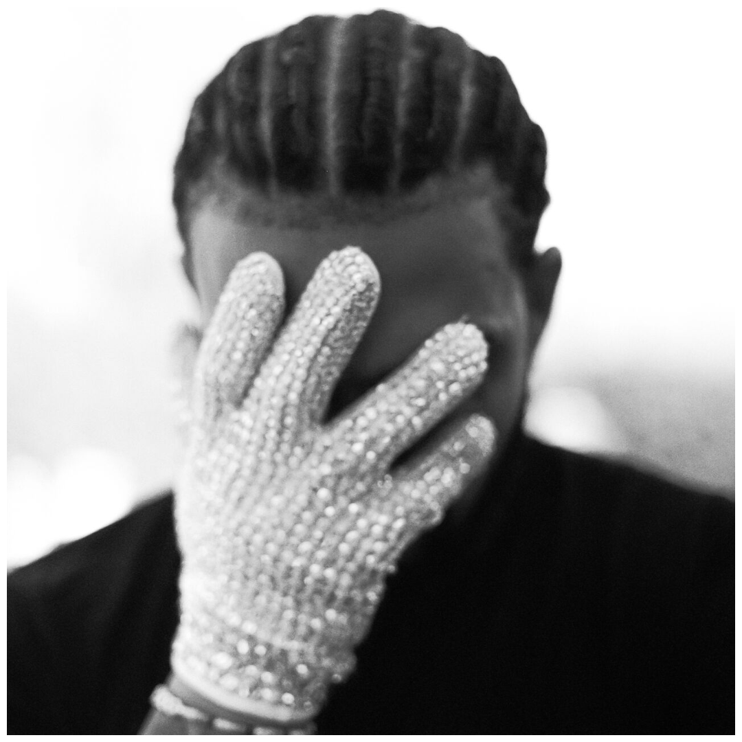 Drake in dark clothing wears an ornate white sequined glove while covering their face with their hand.