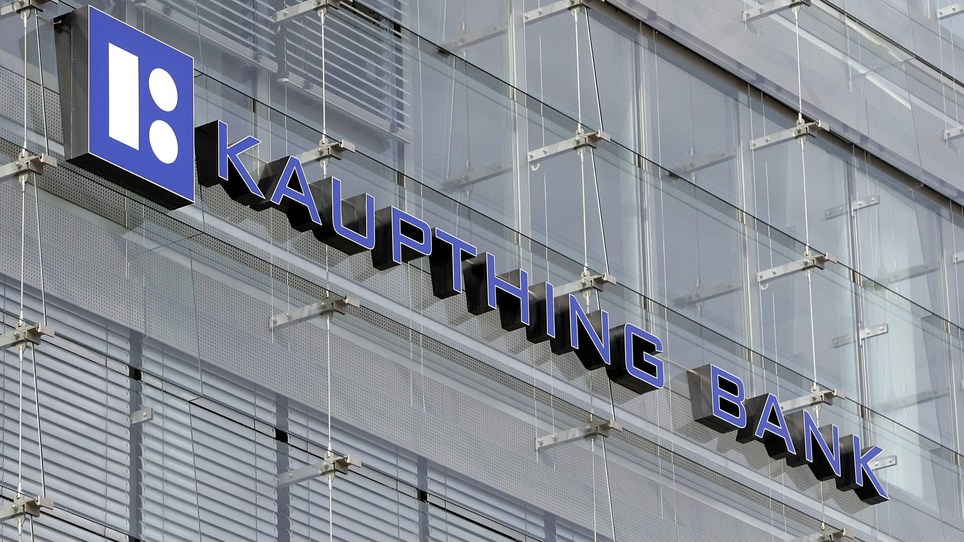 The exterior of Kaupthing Bank's building with the bank's name and logo mounted on a glass facade.