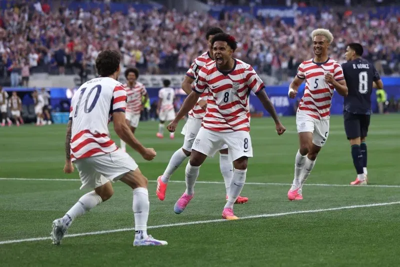 USA players in red and white striped kits celebrating a goal on the pitch at the FIFA World Cup.