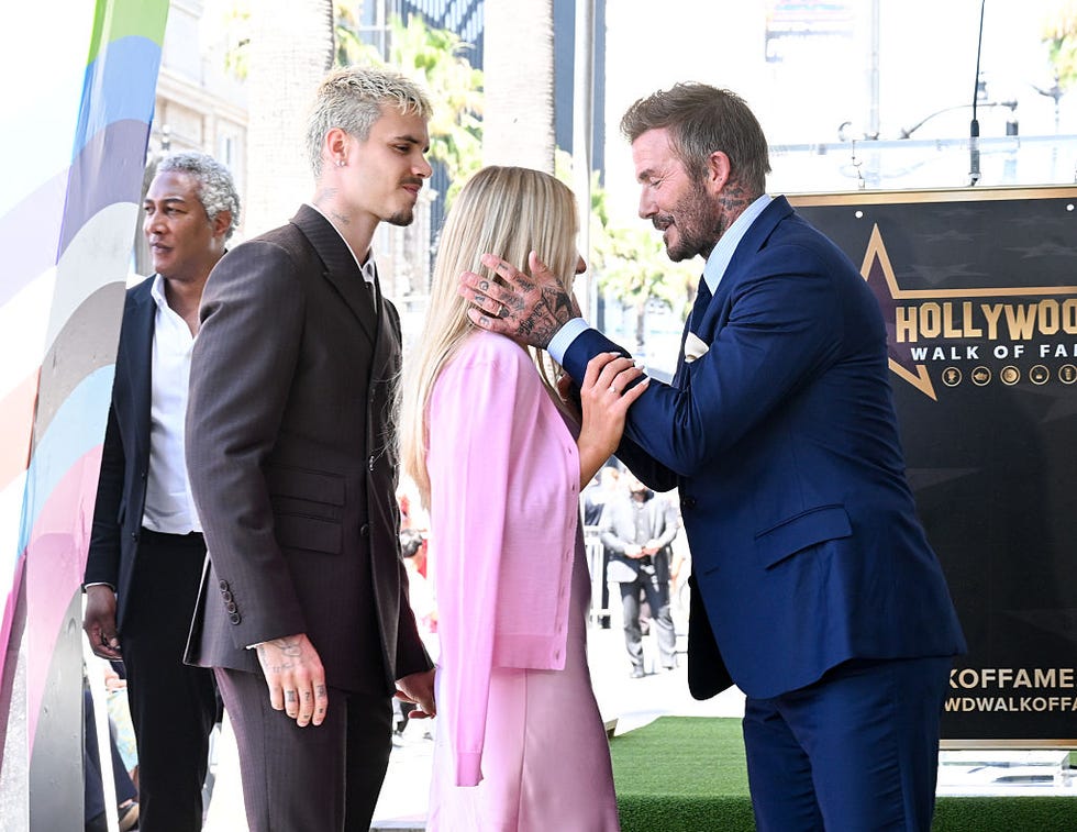 David Beckham leaning in to kiss Harper Beckham on the head while Romeo Beckham stands alongside them at the Hollywood Walk of Fame ceremony.