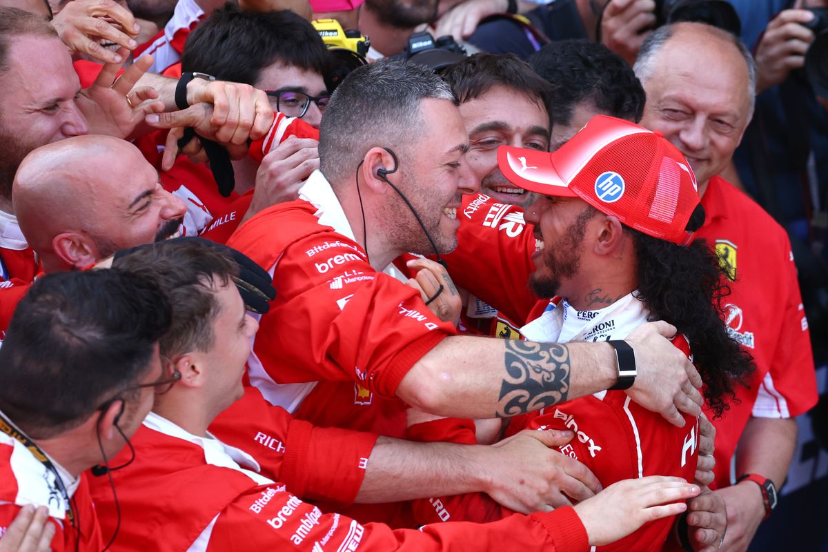Lewis Hamilton and Ferrari F1 team members celebrate together in red uniforms after a race victory.