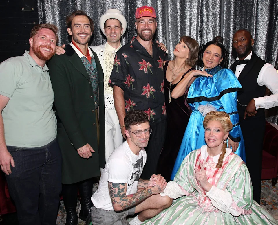 A group of nine people pose together at a formal event with a silver sequined backdrop, dressed in various outfits.