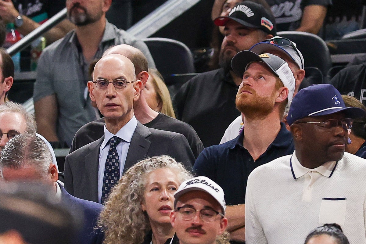 Spectators watch a sports event from courtside seats, including a man in a suit and glasses and others wearing casual attire.