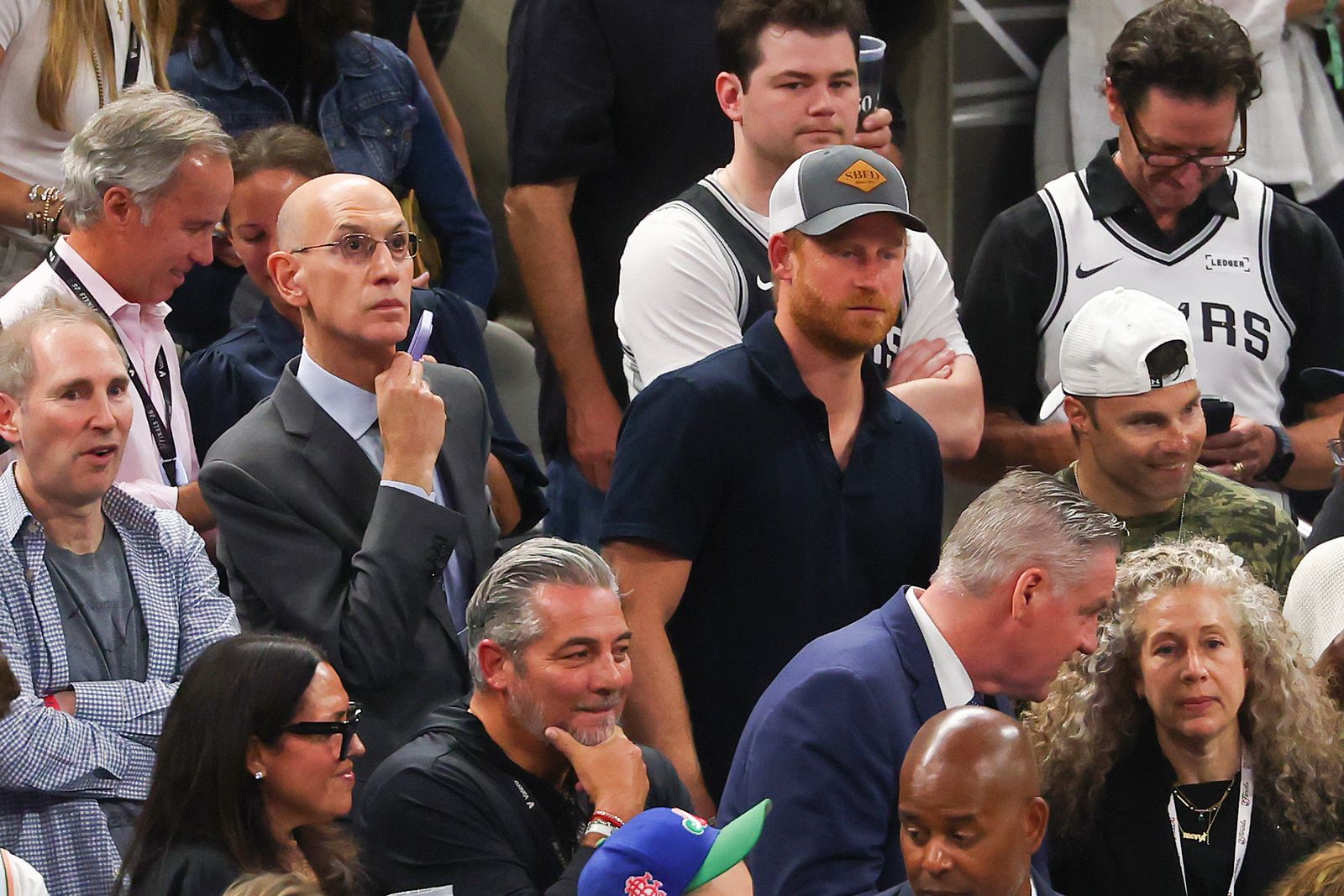 A crowd of spectators watches intently during what appears to be a sporting event, with various audience members in casual and formal attire.