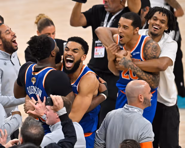 New York Knicks players in blue and orange jerseys celebrating together on the court after winning Game 5.