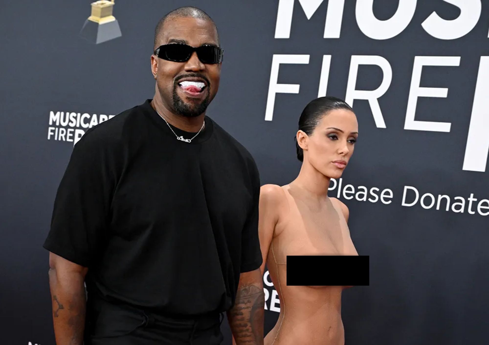Kanye West in black t-shirt and sunglasses holding hands with Bianca Censori in a skintight sheer bodysuit