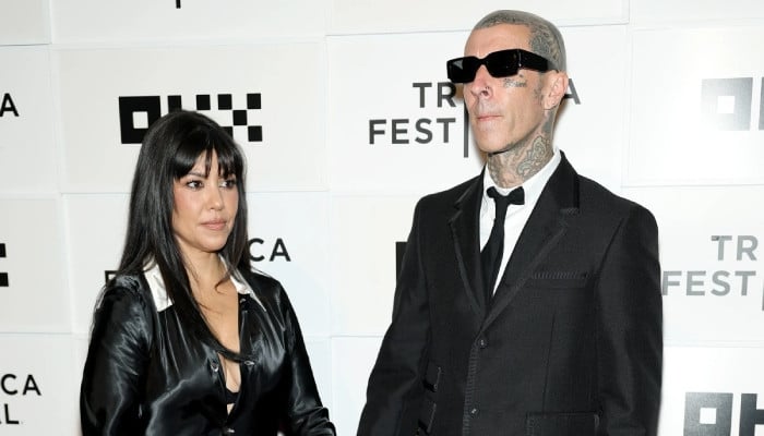 Kourtney Kardashian and Travis Barker in black formal attire at a Tribeca Film Festival event on a white step-and-repeat backdrop.
