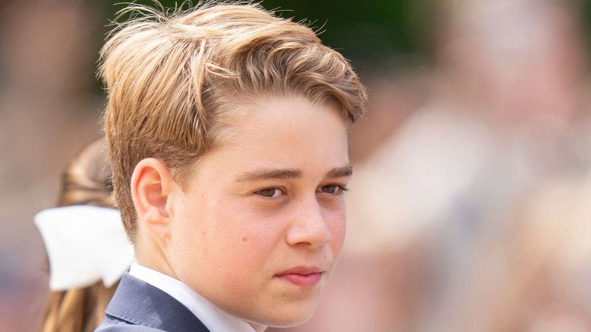 Prince George in formal attire with a white collar and dark jacket, looking to the side with a serious expression.
