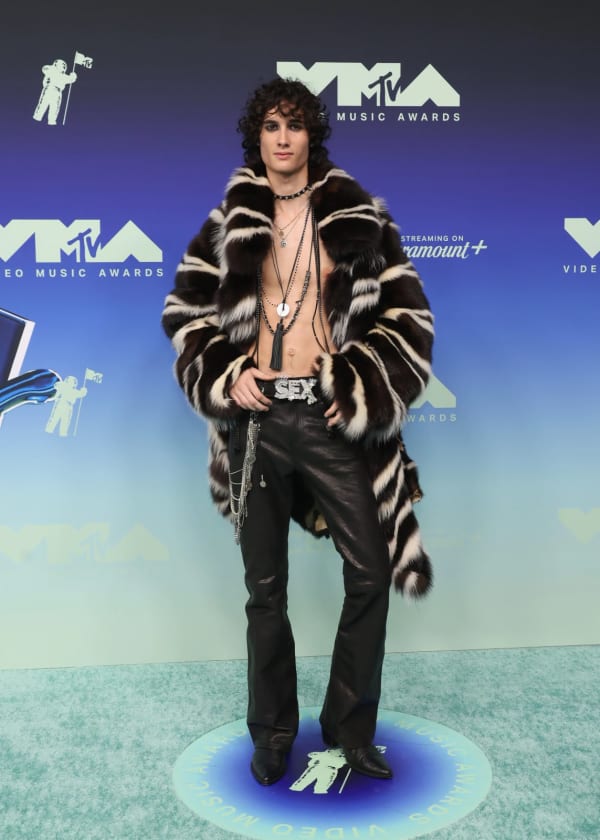 Sombr brings full rock-star energy to the 2026 MTV VMAs blue carpet at the Peacock Theater in Los Angeles, going shirtless beneath a custom ERL faux-fur skunk coat paired with deadstock leather flares and a crystal-encrusted "SEX" belt buckle.