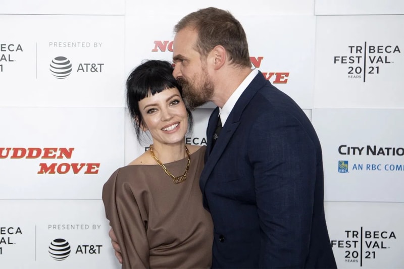 David Harbour speaking at a press event, wearing a dark suit and smiling at the camera