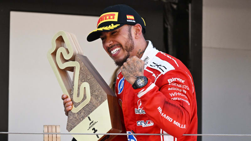 Lewis Hamilton celebrating in parc fermé at the Barcelona-Catalunya Circuit, wearing his red Ferrari race suit and holding a trophy after winning the Spanish Grand Prix