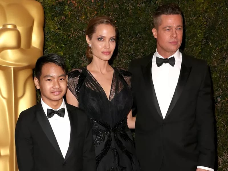 Maddox Jolie-Pitt, Angelina Jolie, and Brad Pitt posing together at an awards event, all dressed in formal black attire with bow ties.