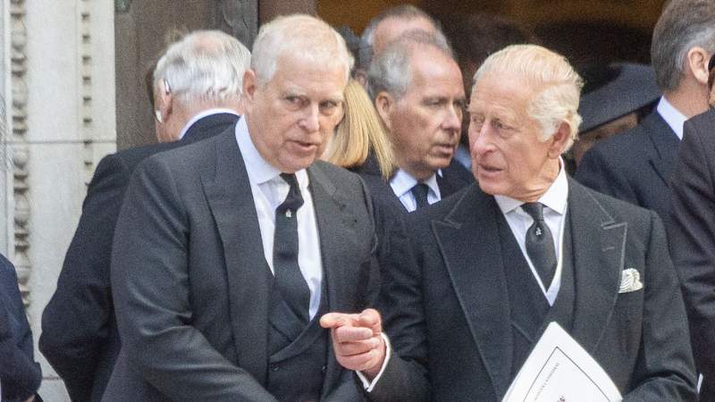 Andrew Mountbatten-Windsor and King Charles in dark suits at a formal event, standing close together among a crowd.
