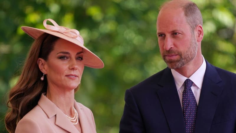 Kate Middleton and Prince William in formal attire stand together outdoors against a blurred green background.