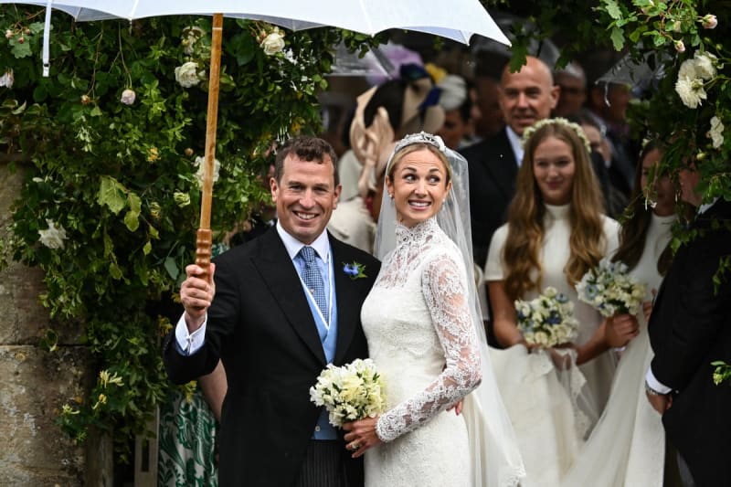 A newlywed couple shares an umbrella during their rainy wedding ceremony, surrounded by white flowers and wedding guests.