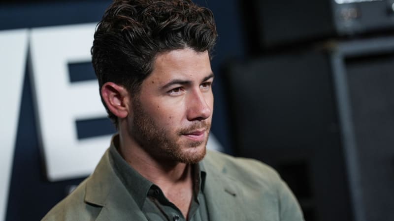 Nick Jonas wears a tan button-up shirt at what appears to be a professional event.