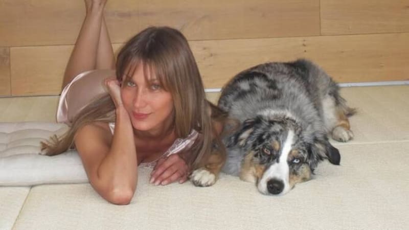 Bella Hadid lying on the floor beside a Australian Shepherd dog, wearing a pink satin top.