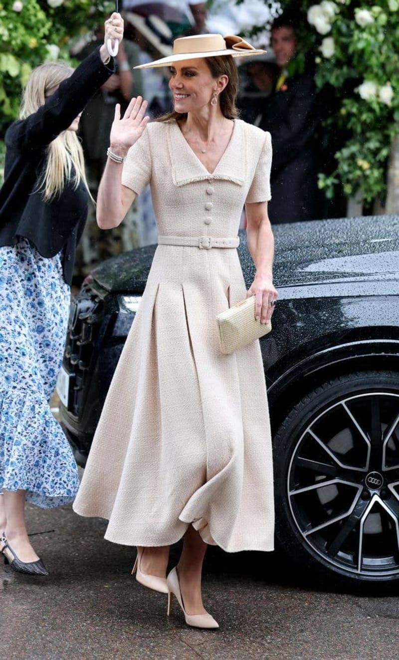 Kate Middleton in a cream-colored dress and wide-brimmed hat waves while standing beside a black car at an outdoor event.