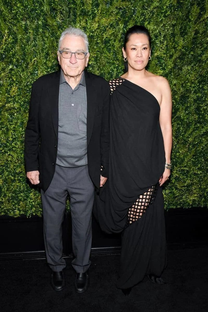 Robert De Niro and Tiffany Chen posing together in front of a green foliage backdrop at a formal event.