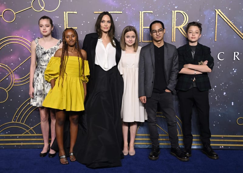 Angelina Jolie poses with her five children together at movie premiere for Eternals with a starry purple and gold backdrop behind them.