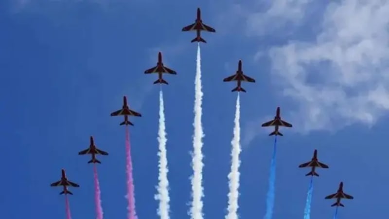 Red Arrows Royal Air Force jets performing an aerobatic display with colored smoke trails in formation against a blue sky.