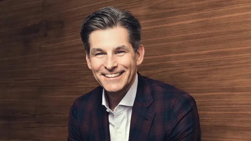 Mike Hopkins in a dark plaid blazer against a wood-panelled background.