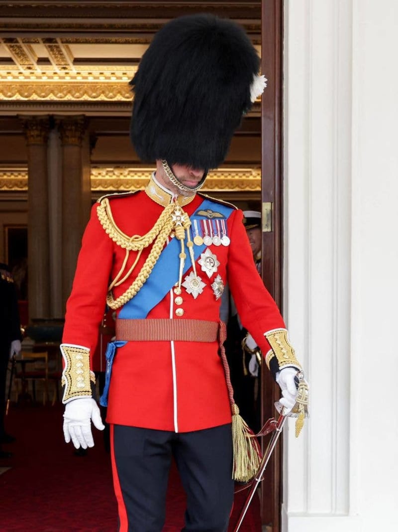 Prince William in full ceremonial dress uniform with bearskin hat, red tunic, blue sash, medals, and white gloves.