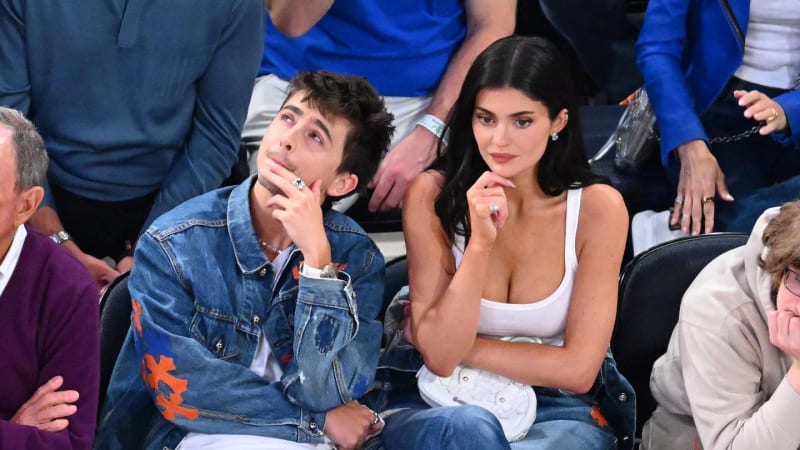 Timothée Chalamet and Kylie Jenner sitting courtside together, both with their hands near their chins, watching a basketball game.