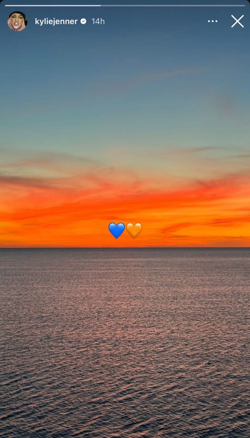 A screenshot of Kylie Jenner's Instagram story showing a sunset over the ocean with blue and orange heart emojis overlaid on the horizon.
