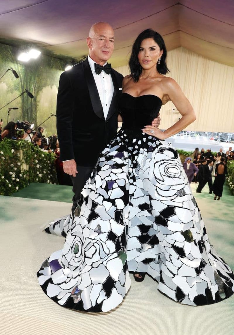 Jeff Bezos in a black tuxedo and Lauren Sanchez in a black and white floral gown pose together at a formal event.