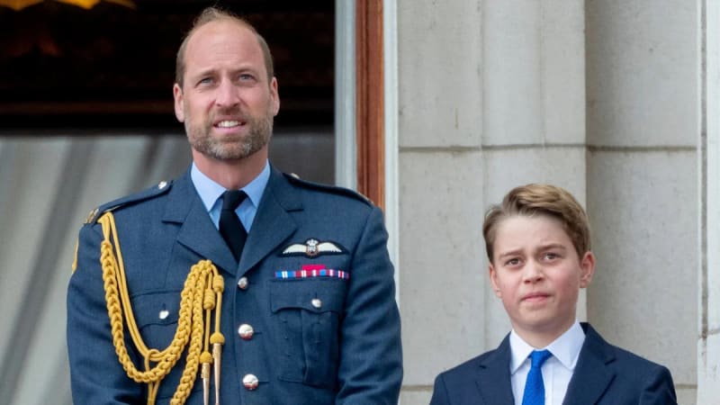 Prince William in blue dress uniform with gold aiguillettes stands beside Prince George in a dark suit with blue tie.